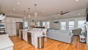 Une cuisine spacieuse avec des meubles blancs, un îlot central, des appareils en acier inoxydable et des luminaires suspendus.