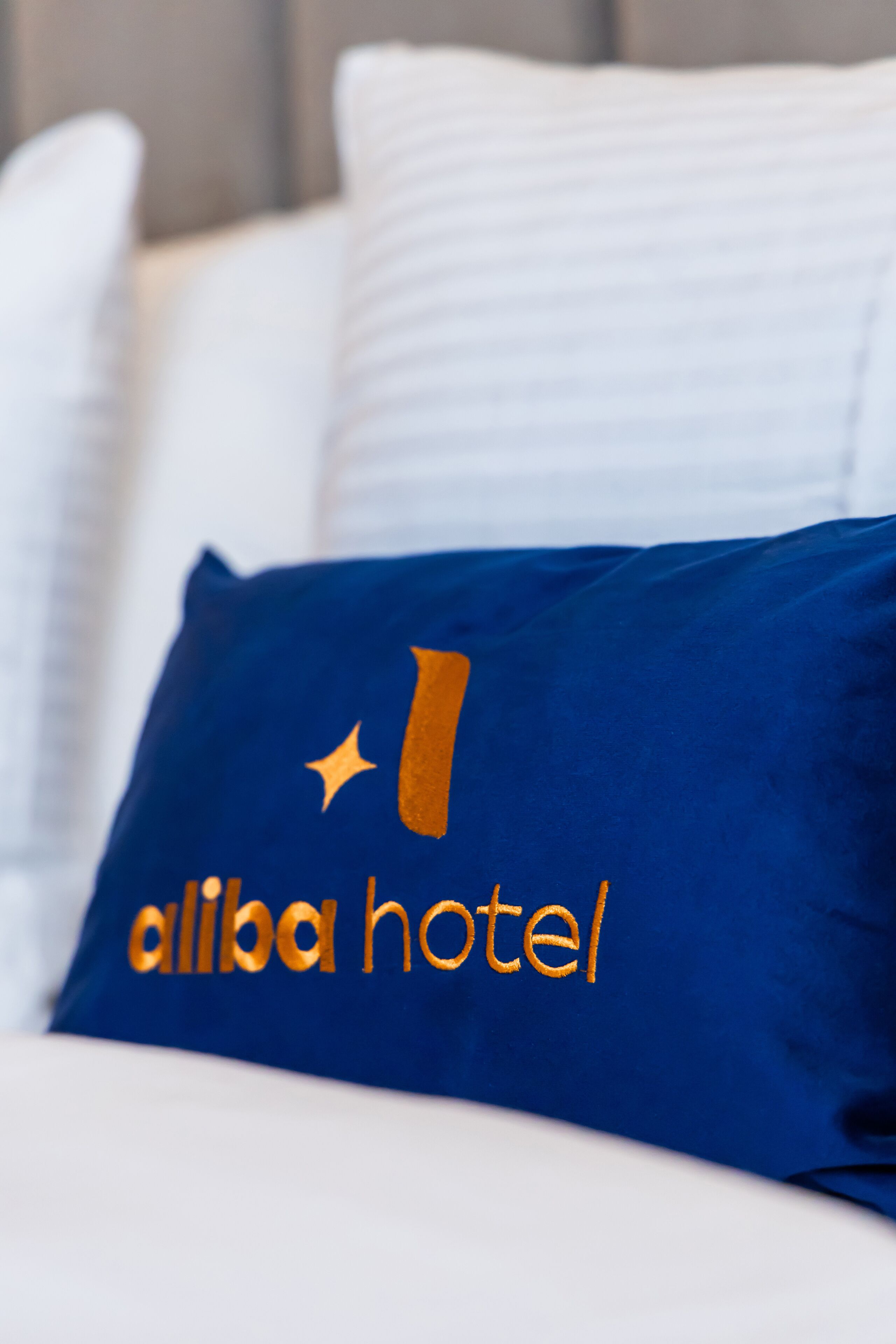 A bed with a blue pillow featuring the Alibaba Hotel logo.