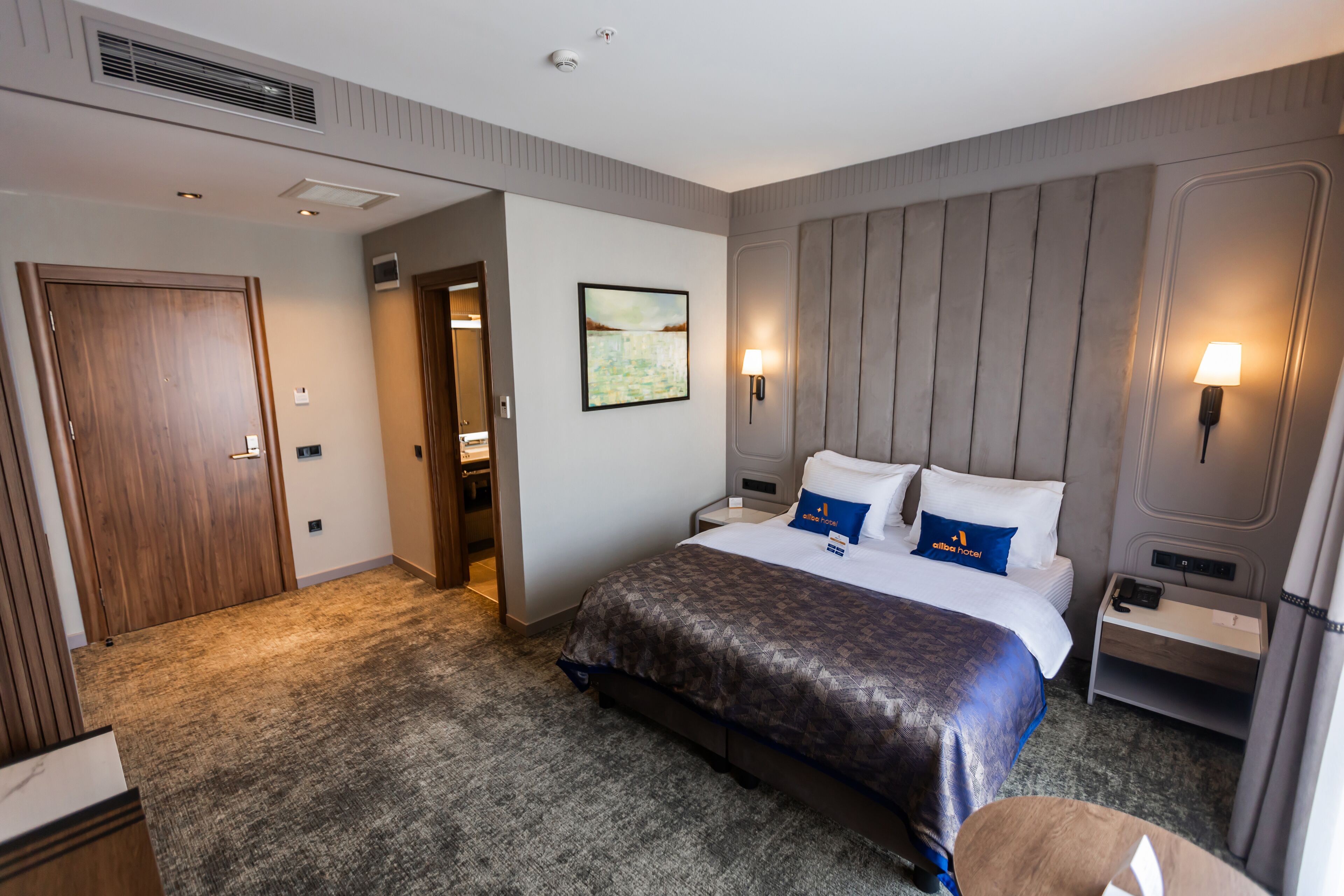 A hotel room with a large bed, a nightstand, a desk, and a door.