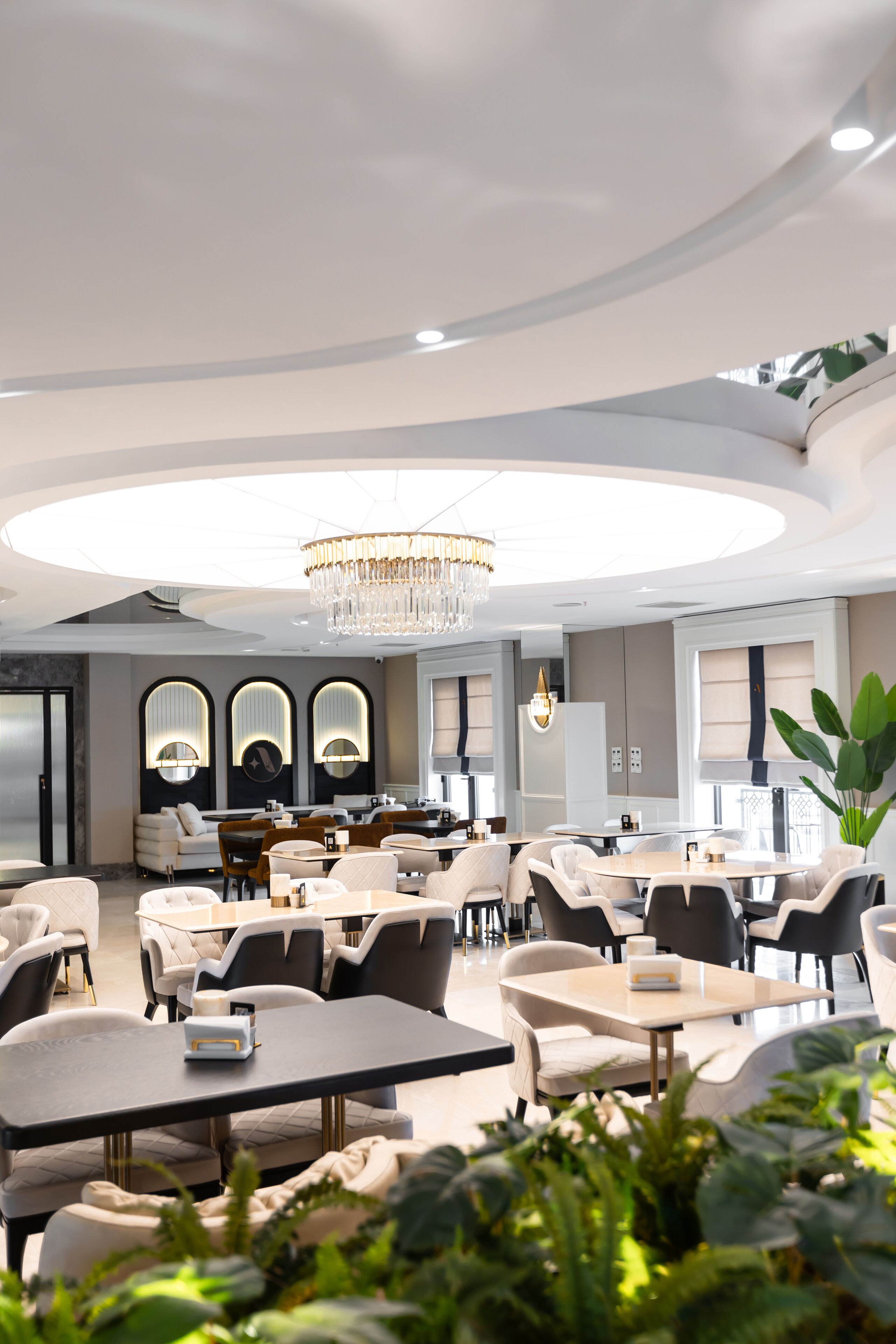 A modern hotel lobby with round tables, comfortable seating, and a large chandelier.