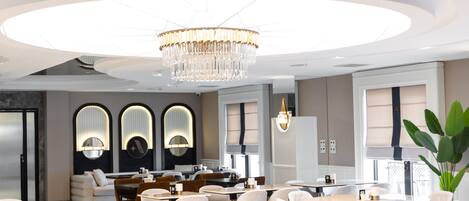 A modern hotel lobby with round tables, comfortable seating, and a large chandelier.