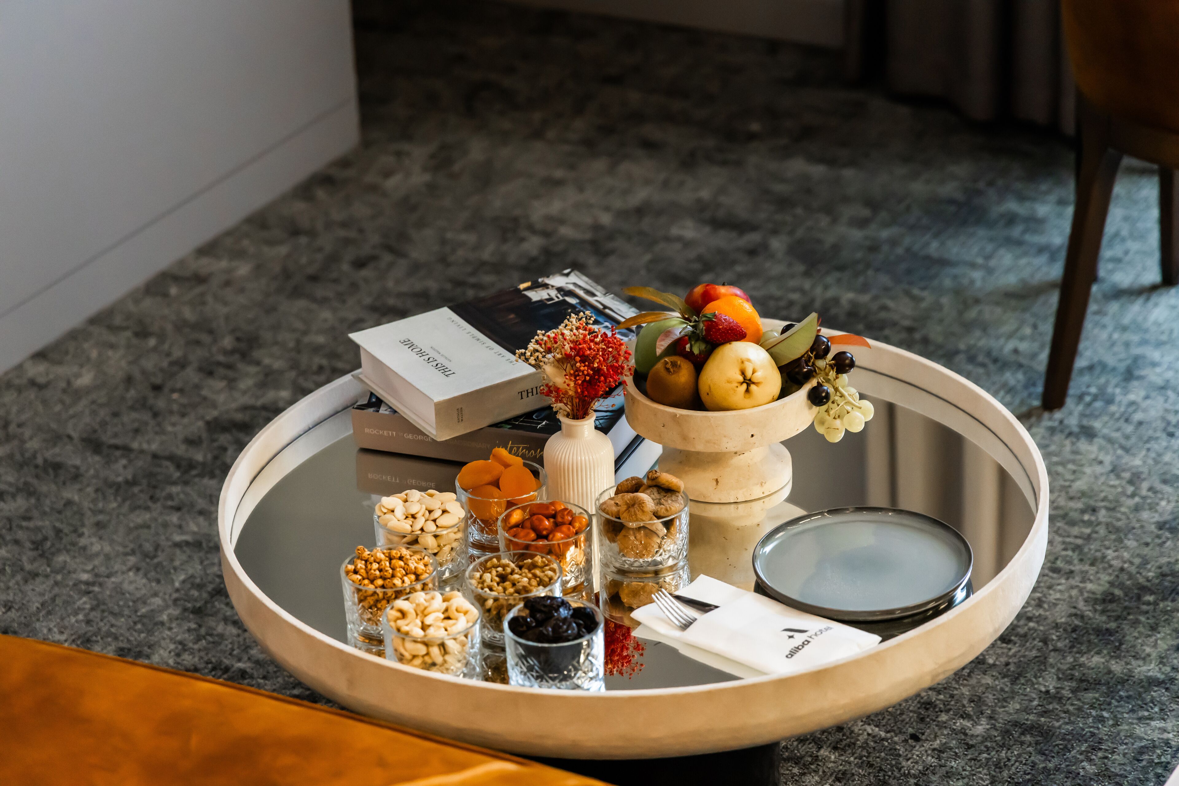 A round table with various food items, a small vase with flowers, and a book.