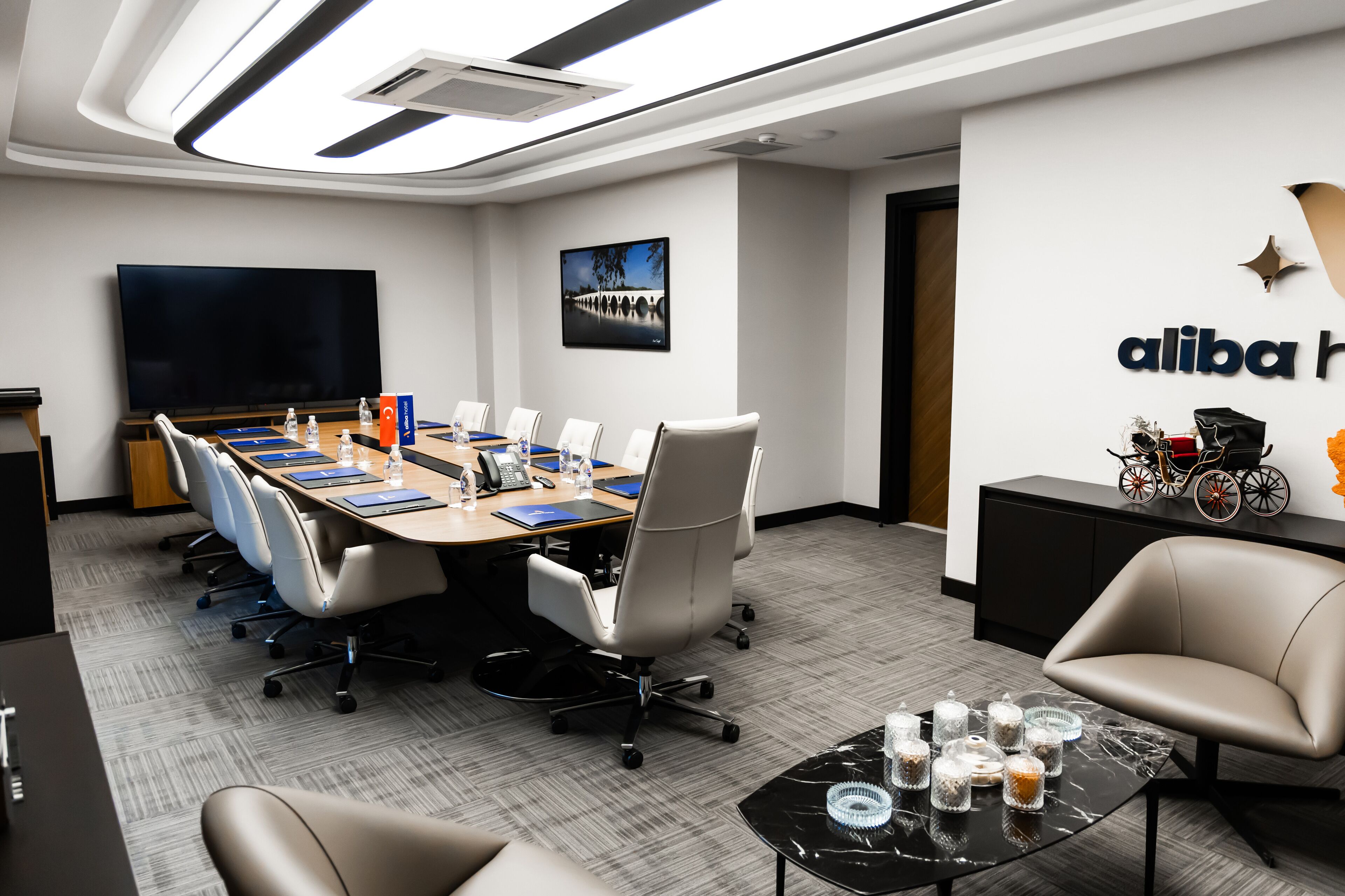 Una sala de conferencias moderna con una larga mesa, sillas, un televisor y una pared con el logotipo de Alibaba.