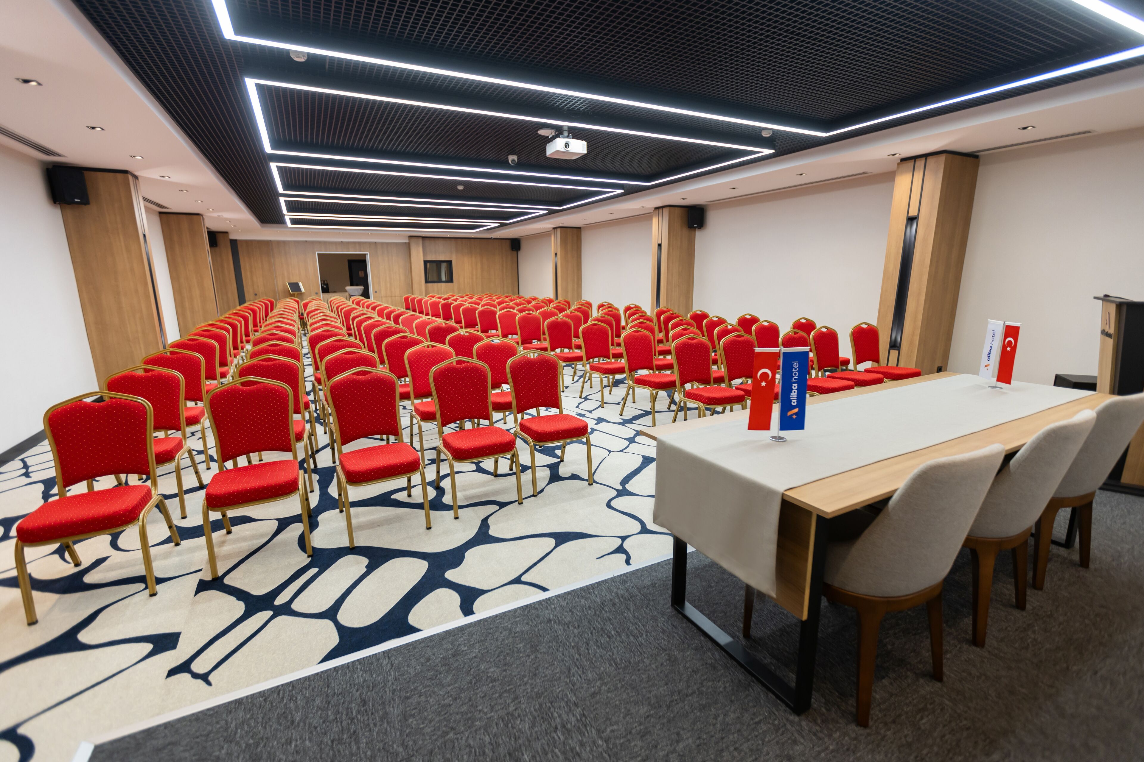 A conference room with rows of red chairs, a long table, and a modern ceiling design.