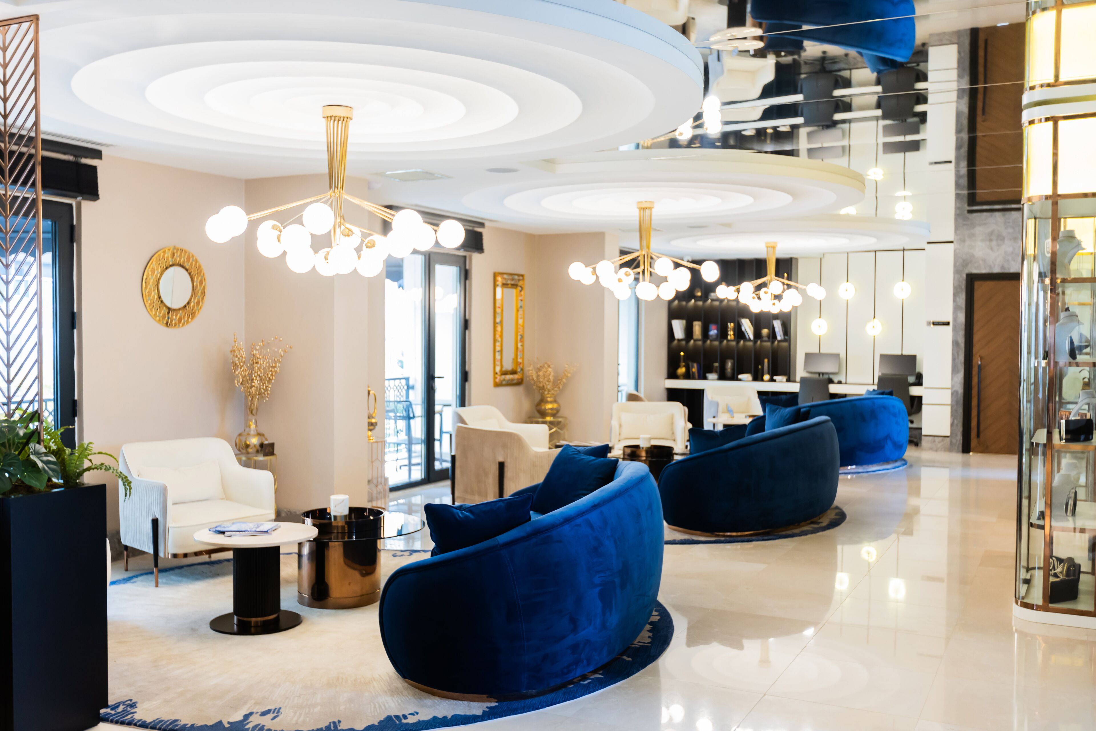 A modern lobby with a white sofa, blue armchairs, and a chandelier.