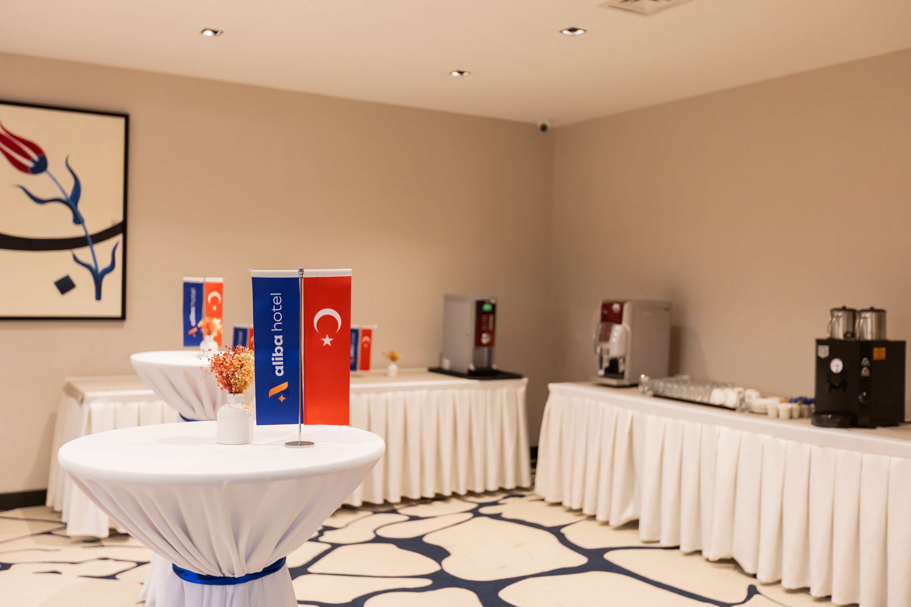 A conference room with round tables, a coffee station, and a wall-mounted artwork.
