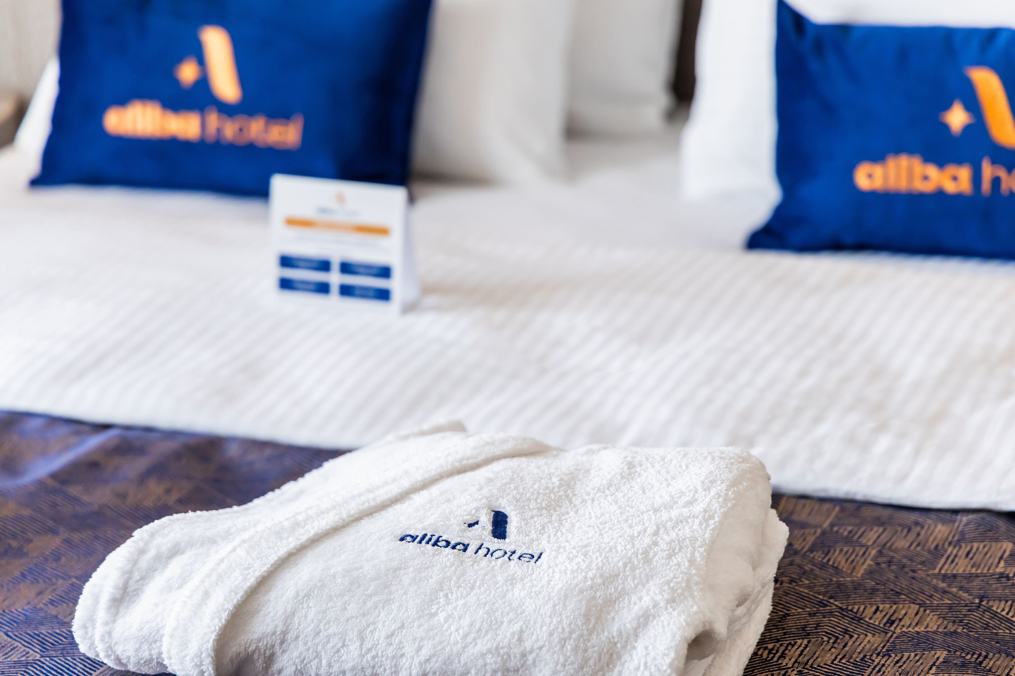 Ein ordentlich bezogenes Bett mit einem weißen Handtuch und Kissen, die das Logo des Alibaba Hotels tragen.