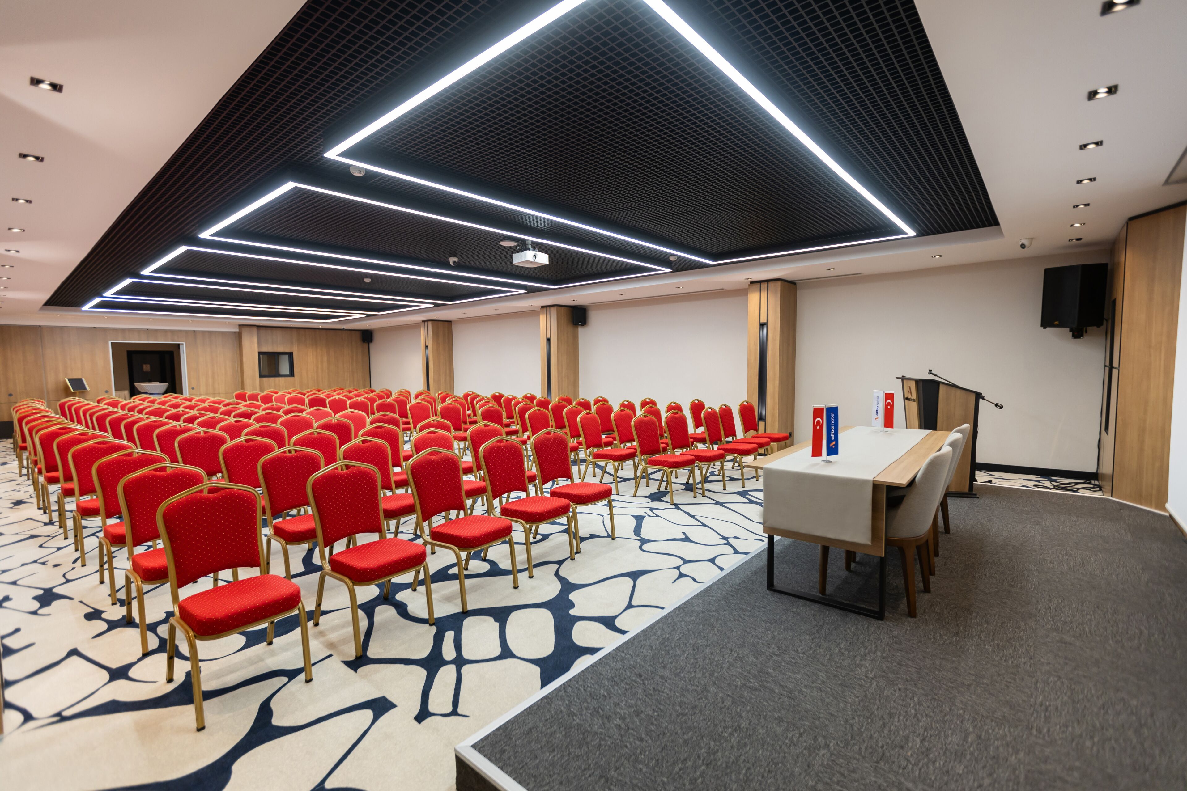 A conference room with rows of red chairs, a white table, and a modern ceiling design.