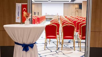 A conference room with a white table, blue ribbon, and a flag. Red chairs are arranged in rows.
