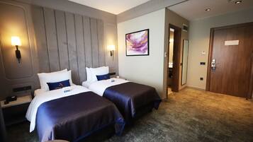 A hotel room with two beds, a large wall-mounted headboard, a painting, and a door with a sign.