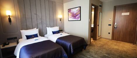 A hotel room with two beds, a large wall-mounted headboard, a painting, and a door with a sign.