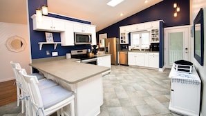 A modern kitchen with white cabinetry, a central island, and a microwave. - Knot A Care, Oceanside House in Emerald Isle, NC! (Emerald Isle)