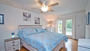 A bedroom with a wooden bed, a nightstand, a ceiling fan, and a large window. - Knot A Care, Oceanside House in Emerald Isle, NC! (Emerald Isle)