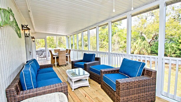 A covered porch with wicker furniture and glass-top tables, overlooking a garden. - Knot A Care, Oceanside House in Emerald Isle, NC! (Emerald Isle)