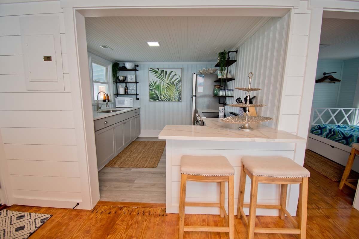 Een moderne keuken met witte kasten, een centraal eiland met krukken, en uitzicht op de aangrenzende woonkamer.