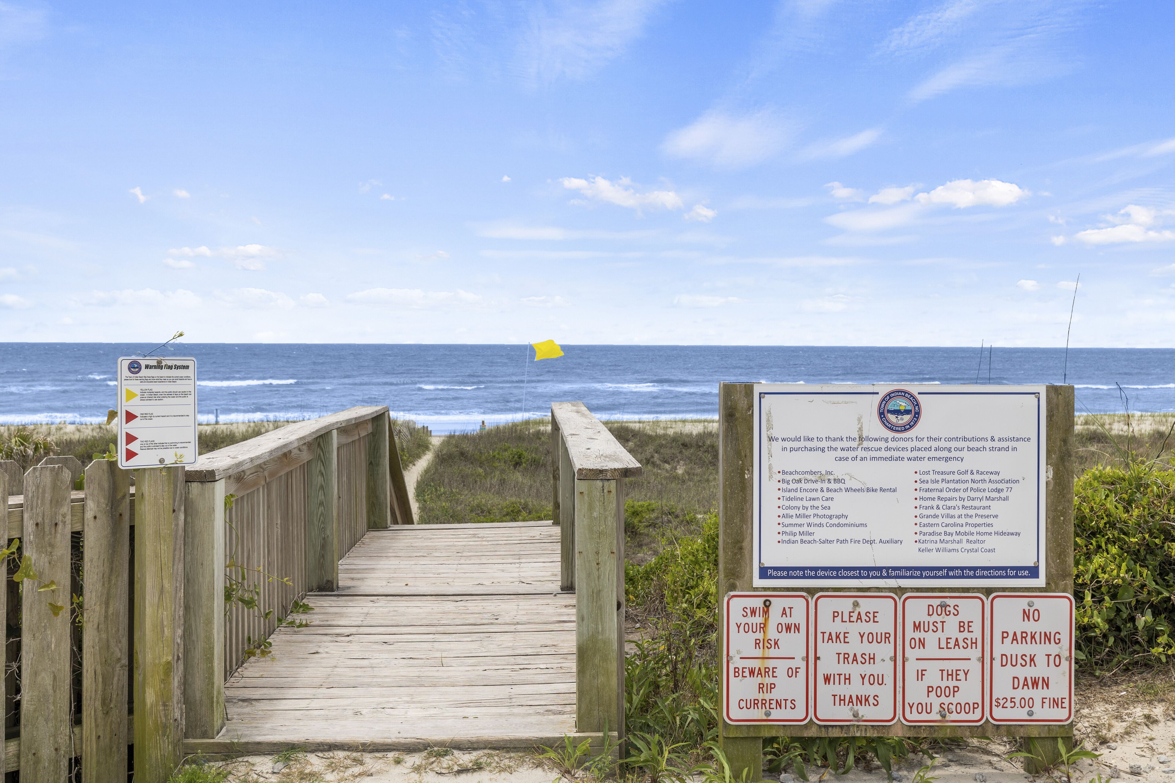 A wooden boardwalk leading to the beach with warning signs and a donation list.