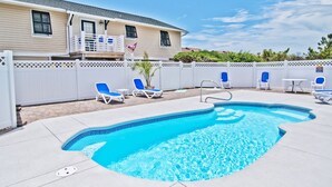 An outdoor swimming pool with lounge chairs and a small table, surrounded by a white fence and a house in the background. - License to Chill, Almost Oceanfront House in Emerald Isle, NC! (Emerald Isle)