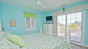 A bedroom with a bed, a dresser, a TV, and a window with a view of the outside. - License to Chill, Almost Oceanfront House in Emerald Isle, NC! (Emerald Isle)