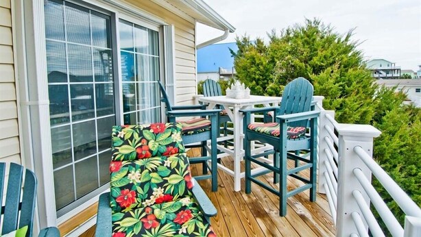 A wooden deck with outdoor furniture, including a bench and chairs, and a white railing. - License to Chill, Almost Oceanfront House in Emerald Isle, NC! (Emerald Isle)