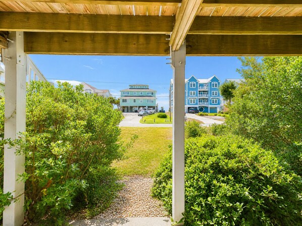 A covered walkway leading to a residential area with a two-story blue house and a light blue house with a garage.
