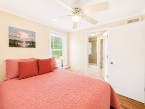 A bedroom with a bed, a ceiling fan, a window with blinds, and a door leading to a bathroom. - Living Under The Rainbow, Almost Oceanfront House in Emerald Isle, NC! (Emerald Isle)