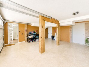 A spacious room with a high ceiling, exposed wooden beams, a white door, and a visible staircase leading to another level. - Living Under The Rainbow, Almost Oceanfront House in Emerald Isle, NC! (Emerald Isle)