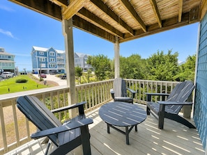 Eine Holzterrasse mit zwei Adirondack-Stühlen und einem kleinen Tisch, mit Blick auf ein Wohngebiet mit Häusern und blauem Himmel.