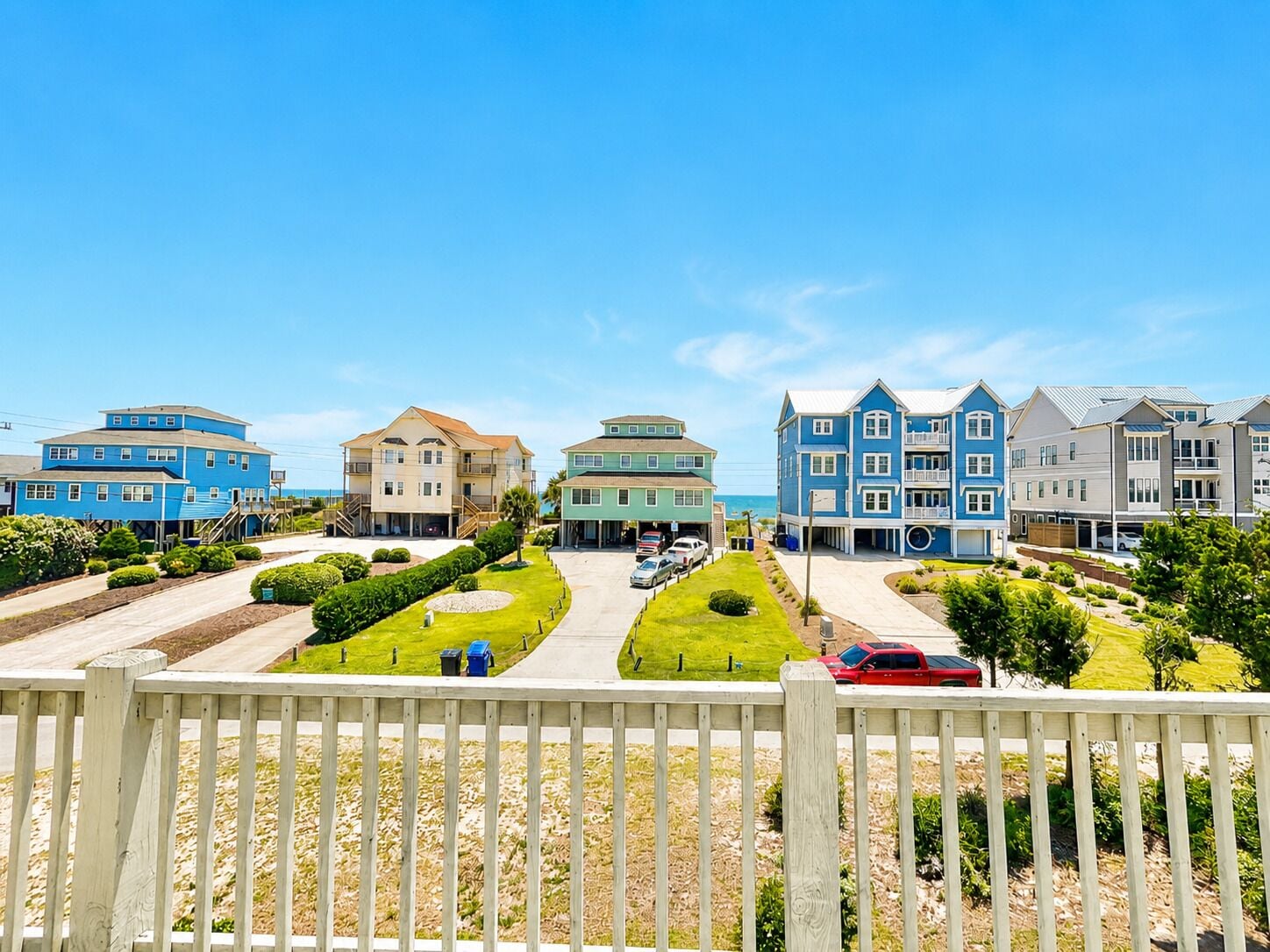 A coastal residential area with multiple two-story houses, a paved driveway, and a wooden fence.