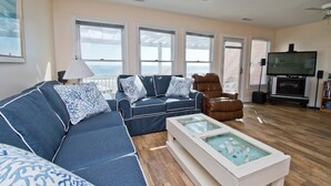 Ein geräumiges Wohnzimmer mit einem blauen Sofa, einem braunen Ledersessel, einem Couchtisch mit Glasplatte und einem Fernseher.