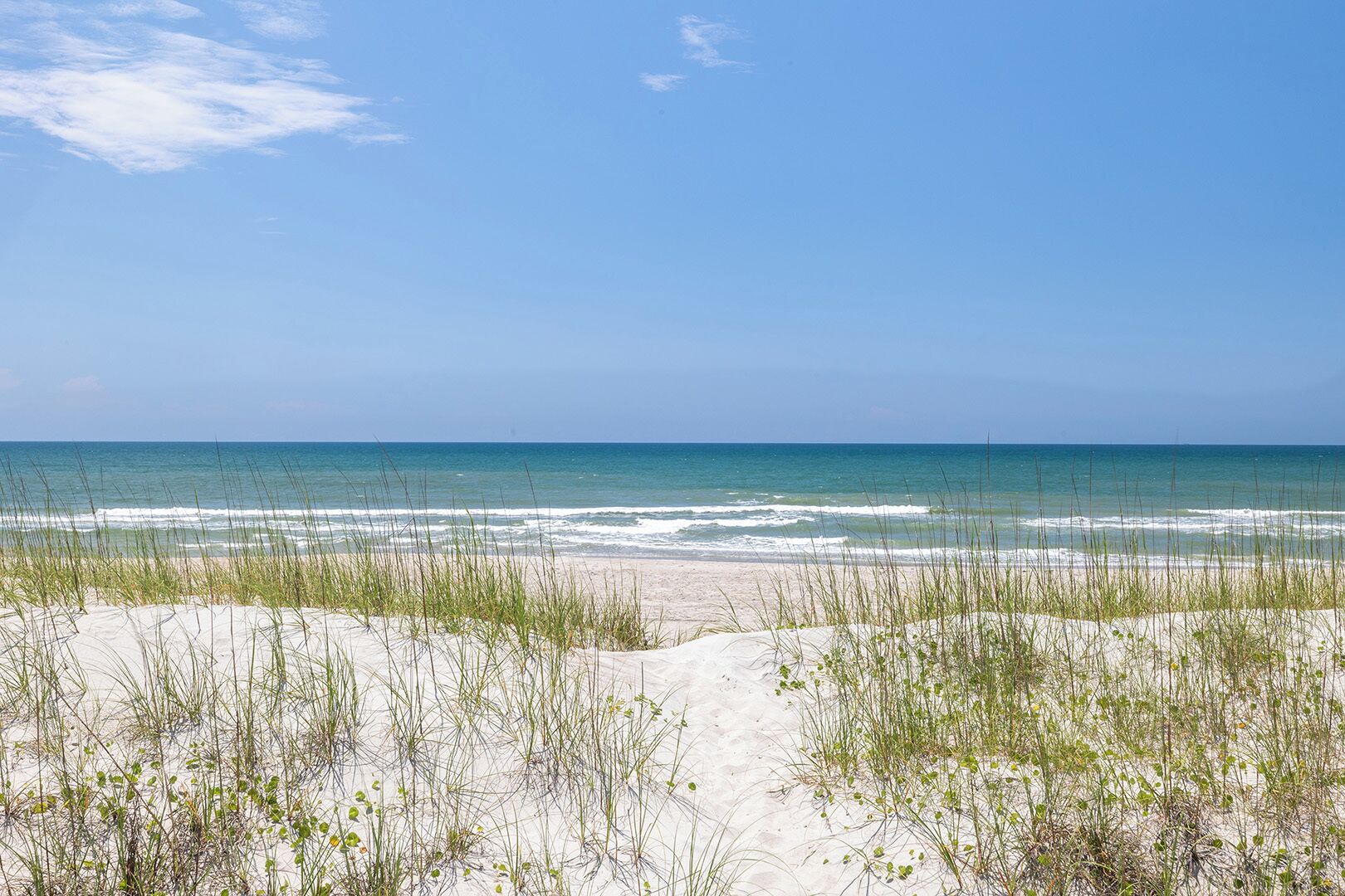 A beach with sand dunes and grass in the foreground, leading to the ocean.