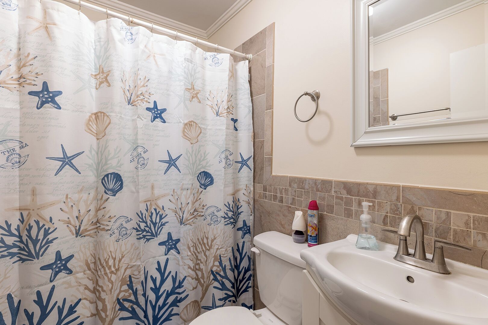 Une salle de bain avec un rideau de douche orné d’un motif sur le thème de la mer, un lavabo avec des articles de toilette et un miroir au-dessus du lavabo.