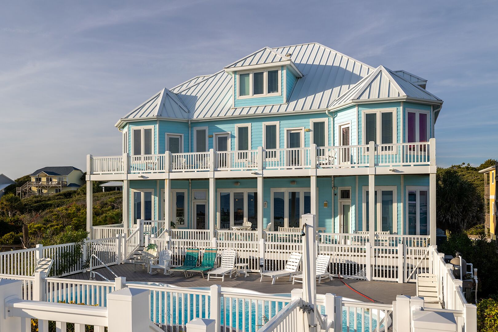 A multi-story house with a pool, balconies, and a deck with lounge chairs.