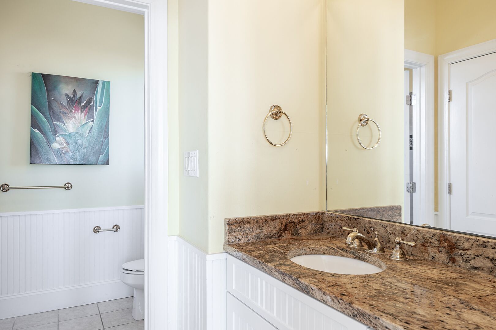 A bathroom with a marble sink, a toilet, and a painting on the wall.