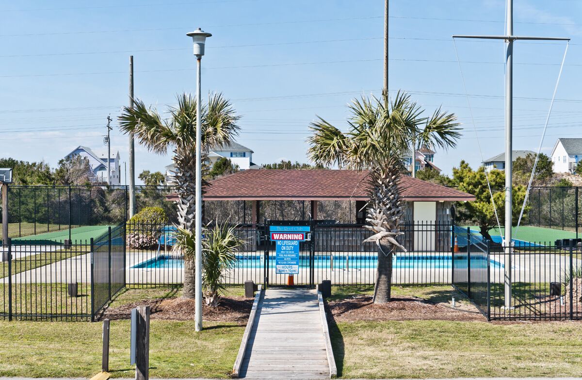A pool area with a wooden deck, palm trees, and a warning sign.