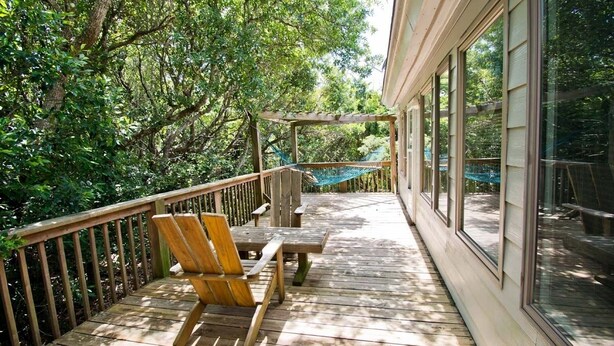 Une terrasse en bois agrémentée d’un hamac et d’un banc, le tout entouré d’une végétation luxuriante.