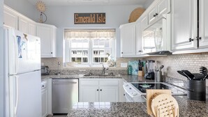 A kitchen with white cabinets, granite countertops, a built-in oven, and a window with a view of a house.
