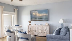 A living room with a ceiling fan, a large framed picture of the ocean, a wooden cabinet with starfish decorations, and a grey sofa.