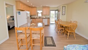 A compact kitchen with wooden cabinets, a central island, and a dining area with wooden chairs. - Nuthin But Sun, Almost Oceanfront House in Emerald Isle, NC! (Emerald Isle)