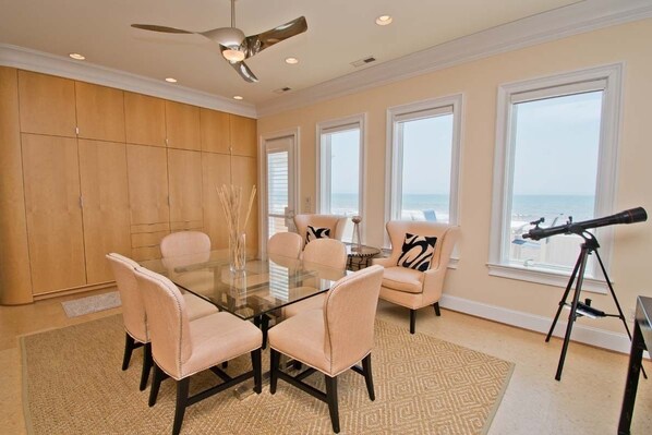 A dining area with a glass table, four chairs, a ceiling fan, and a telescope.