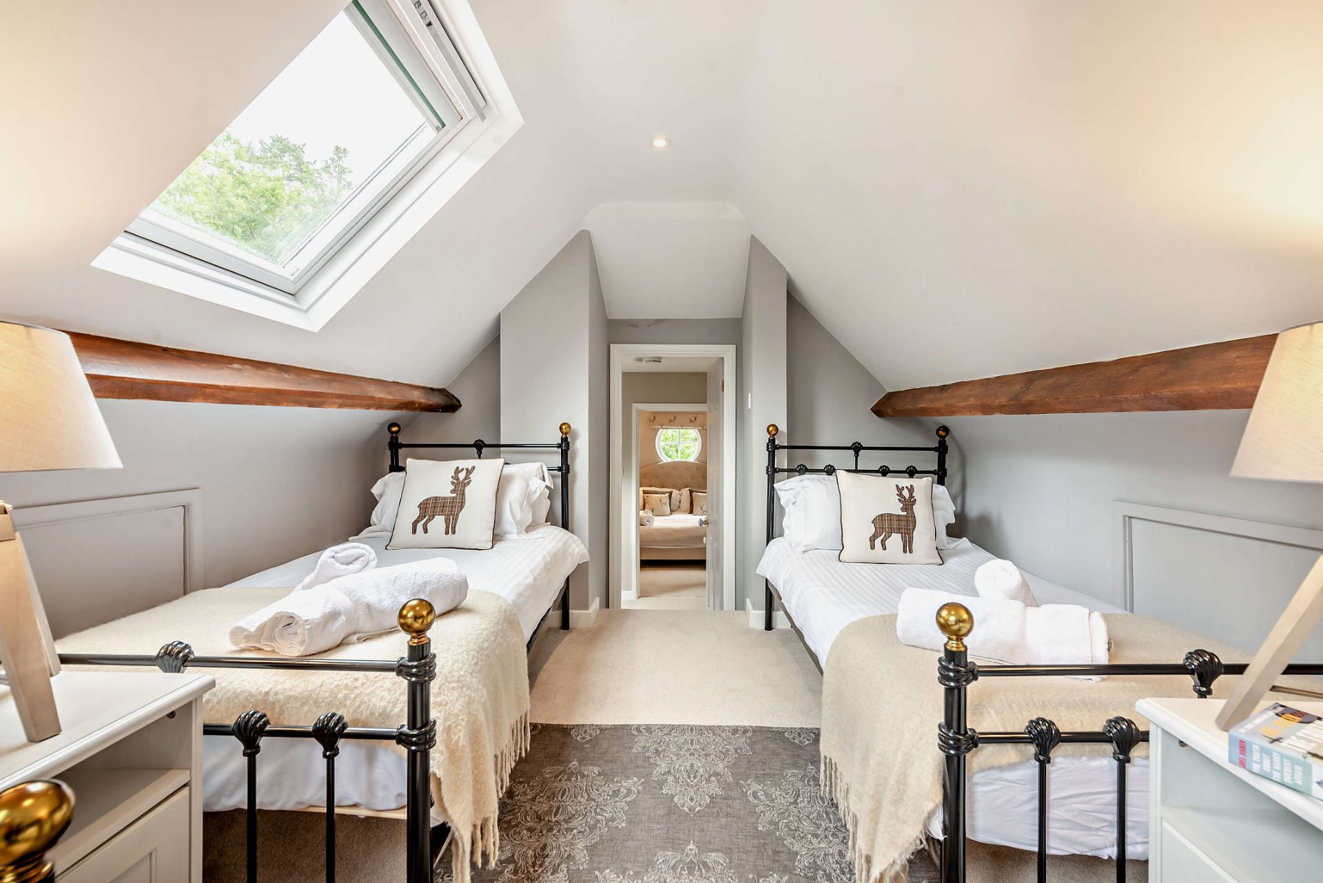A bedroom with two beds, a skylight, and a view of another room.