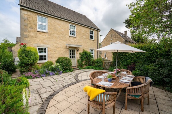 A stone house with a patio, outdoor dining set, and lush garden.