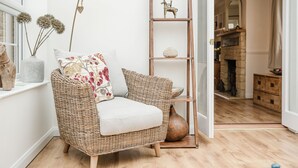 Un divano in vimini con un cuscino, una scaffalatura in legno alta con un oggetto decorativo e un vaso sul pavimento.