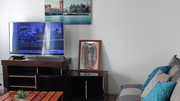 Una sala de estar con televisor de pantalla plana, una mesa de centro de madera, un sofá y un cuadro de un paisaje urbano.