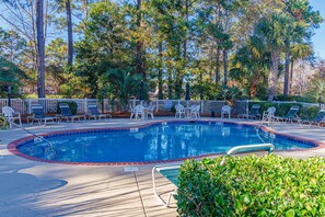 A swimming pool with lounge chairs and a fenced area, surrounded by trees.