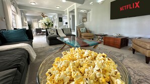 A spacious living room with a large glass coffee table filled with popcorn, a comfortable sofa, a leather armchair, and a Netflix sign on the wall. - The Lauren Taylor Villa - Tobago


 (Lowlands)