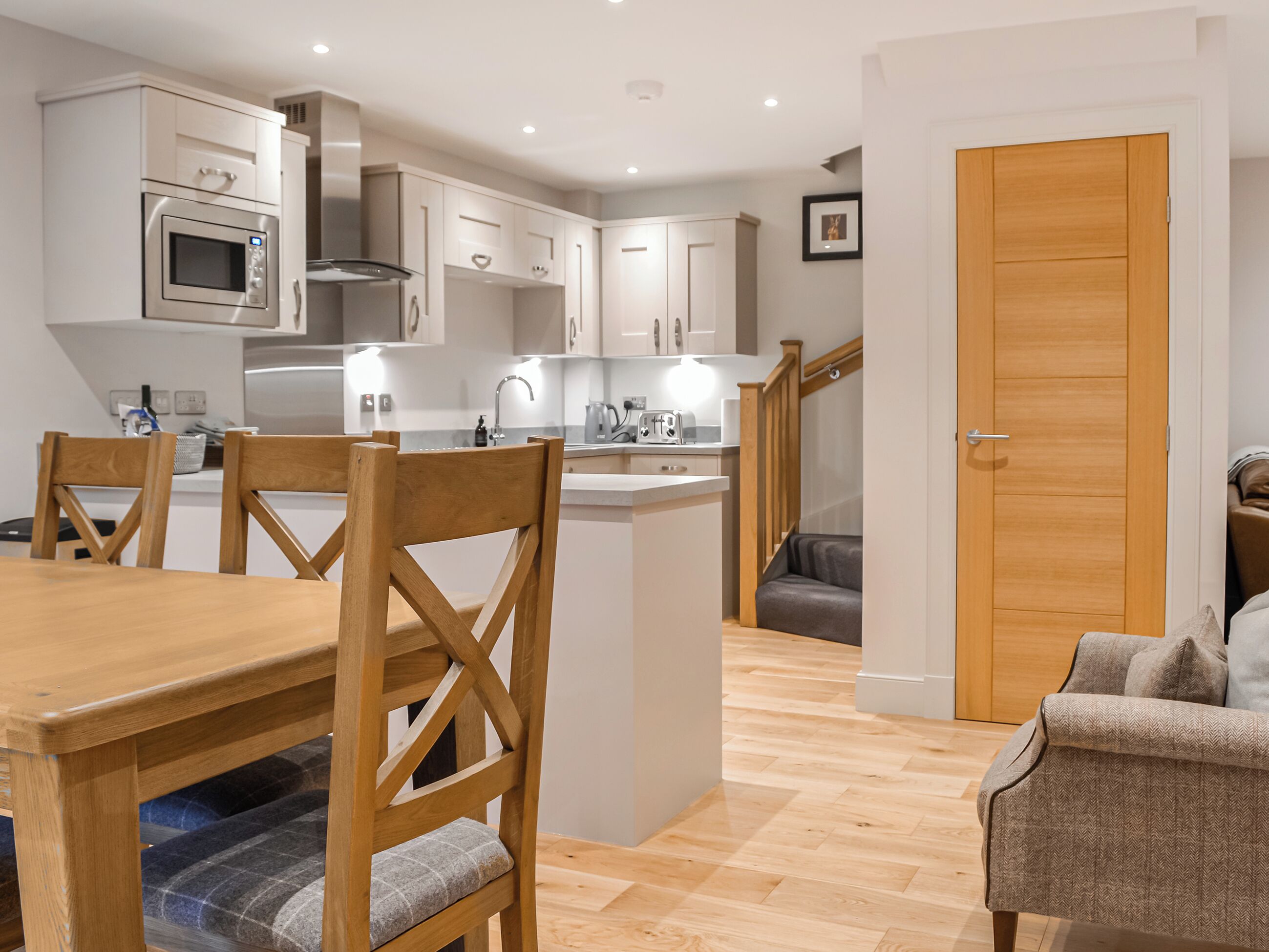 A modern kitchen with white cabinets, a built-in oven, and a dining area with wooden chairs and a table.