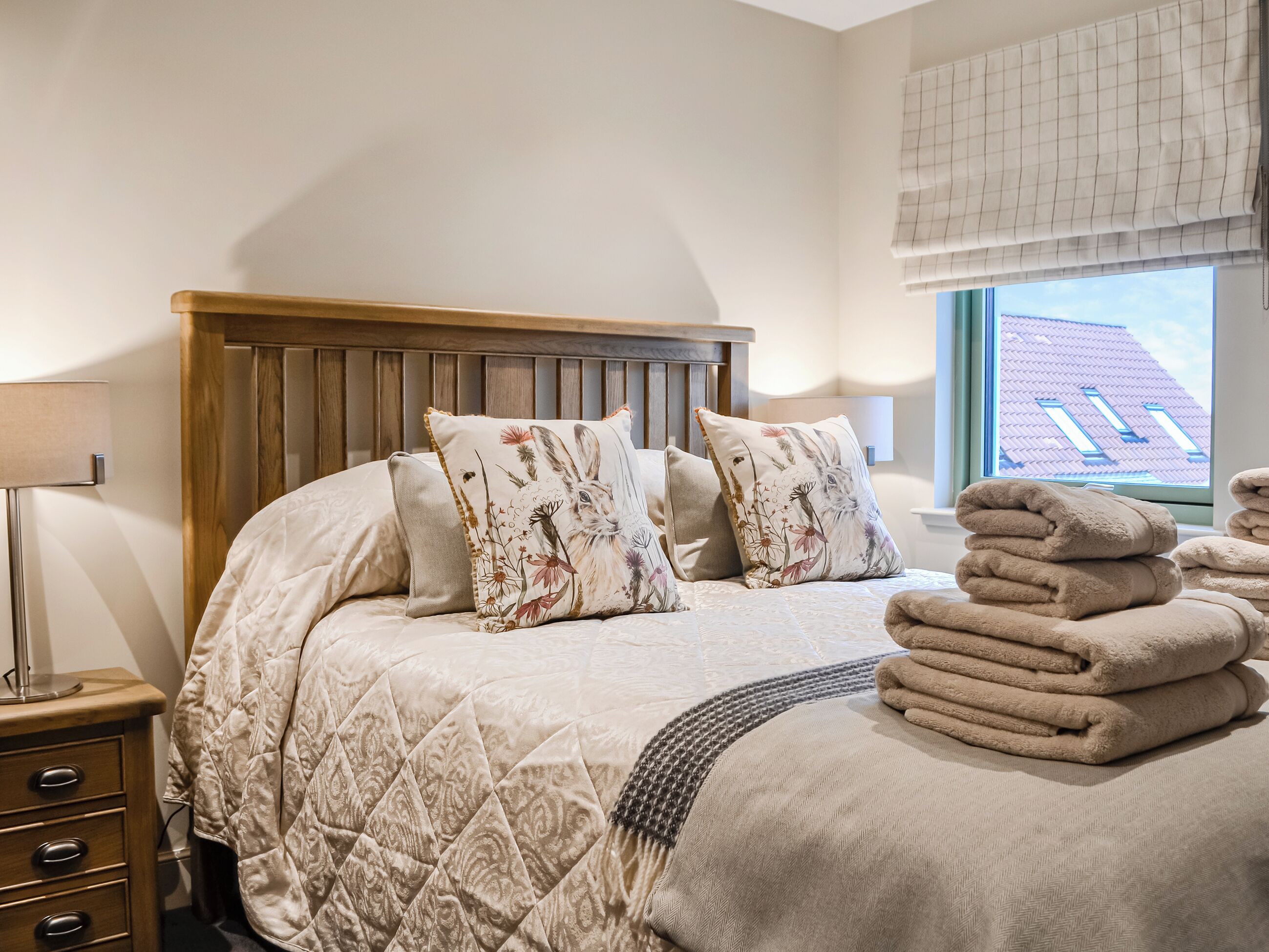 A neatly made bed with patterned pillows, a bedside lamp, and a stack of towels.