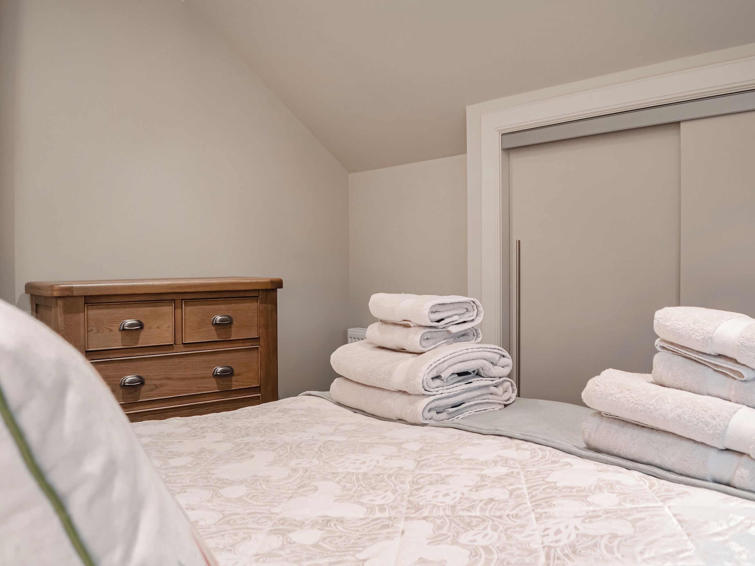 Ein Schlafzimmer mit einem Bett, einer Holzkommode und einem Stapel gefalteter Handtücher.