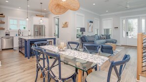A modern kitchen with a central island, dining area with a glass table, and a living room with a sofa and chairs. - Tigh Na Mara is a Porch Lover’s Paradise in Orange Beach, AL (Orange Beach)