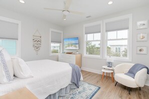 A bedroom with a bed, a chair, a dresser, a television, and a window with blinds.